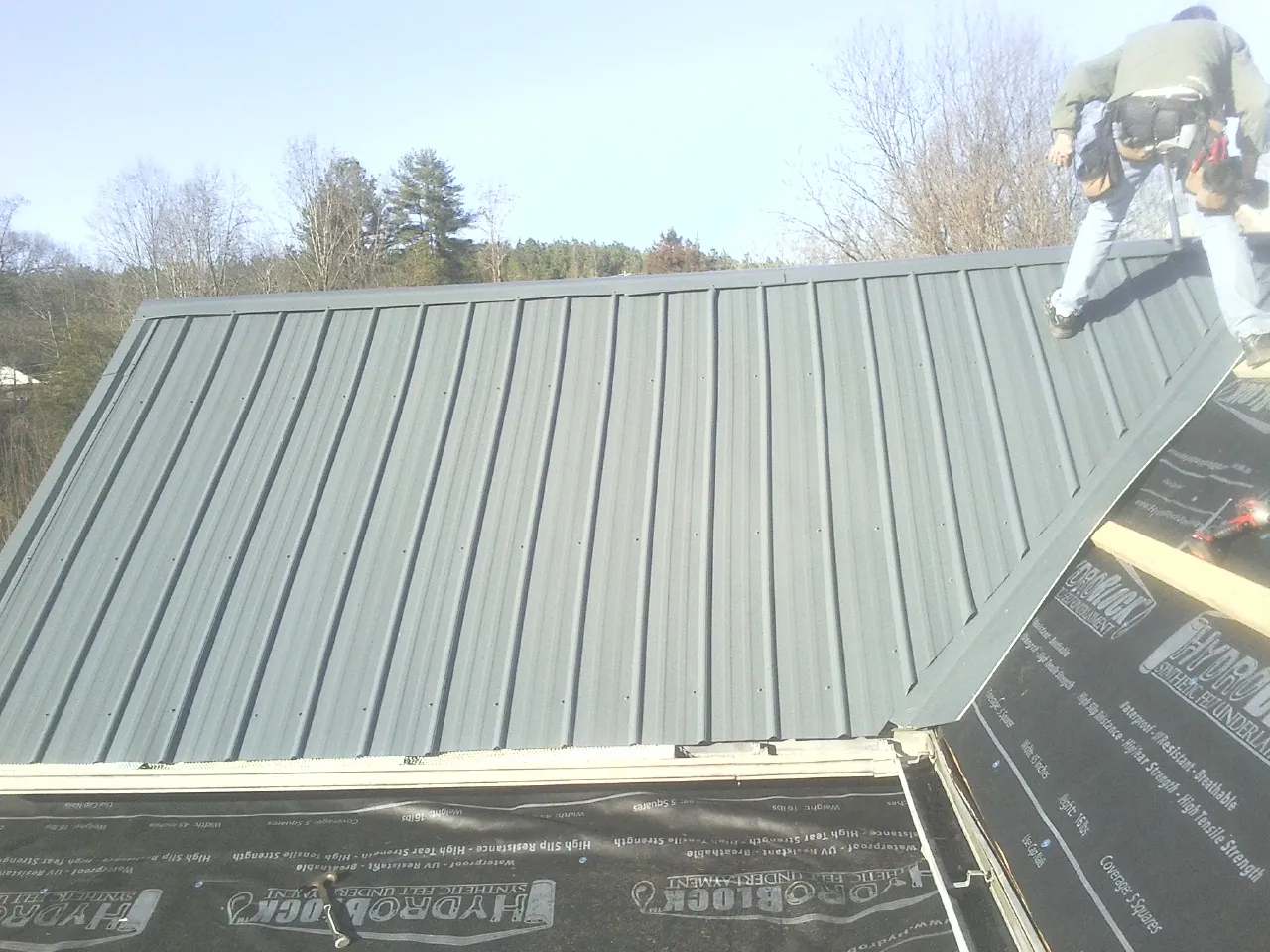 Crew installing dark green standing seam panels over synthetic underlayment in Tyrone