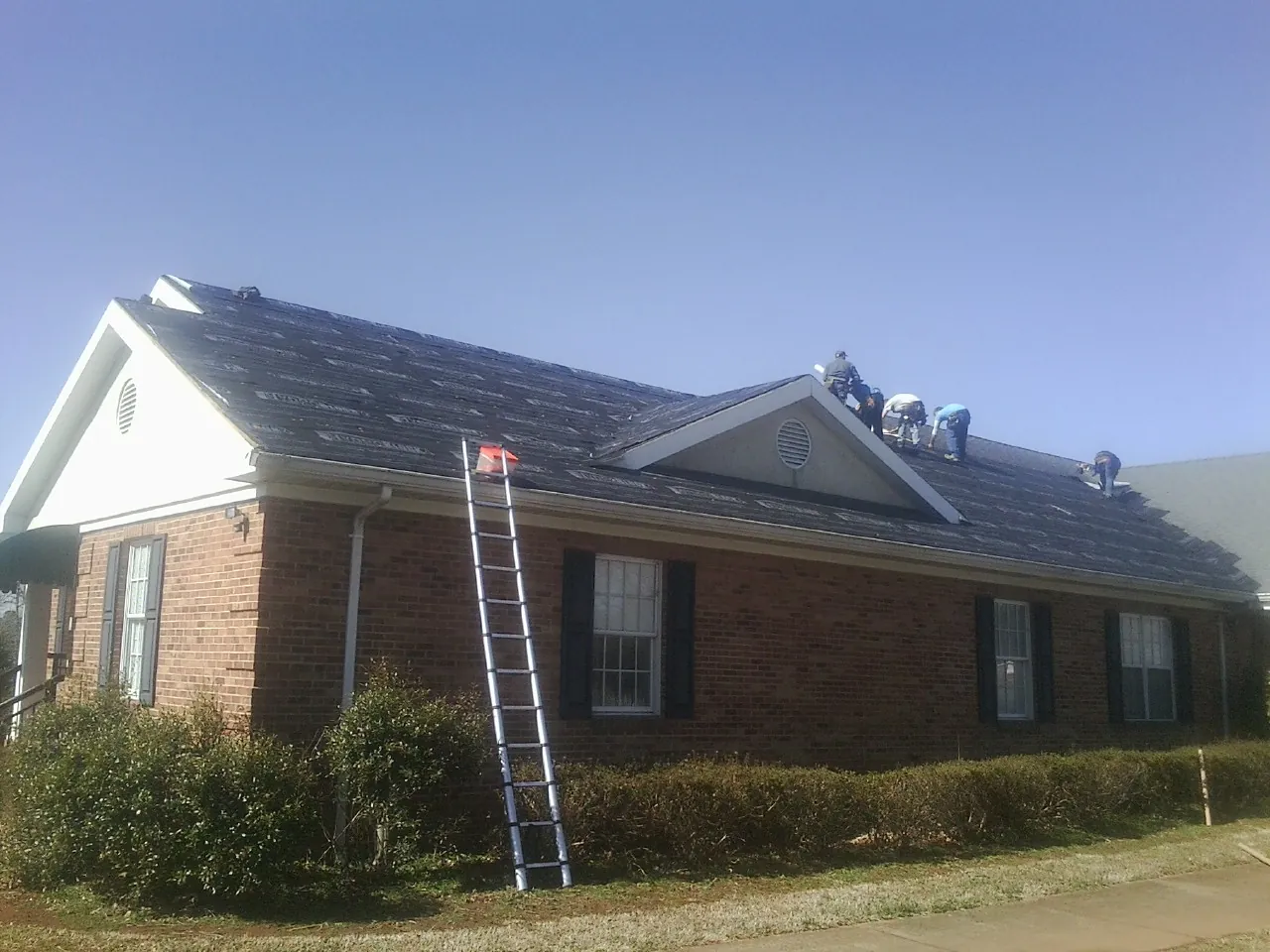 Crew tearing shingles off a brick ranch roof with a ladder set — Metal Roof Repair work by our crew in Tyrone