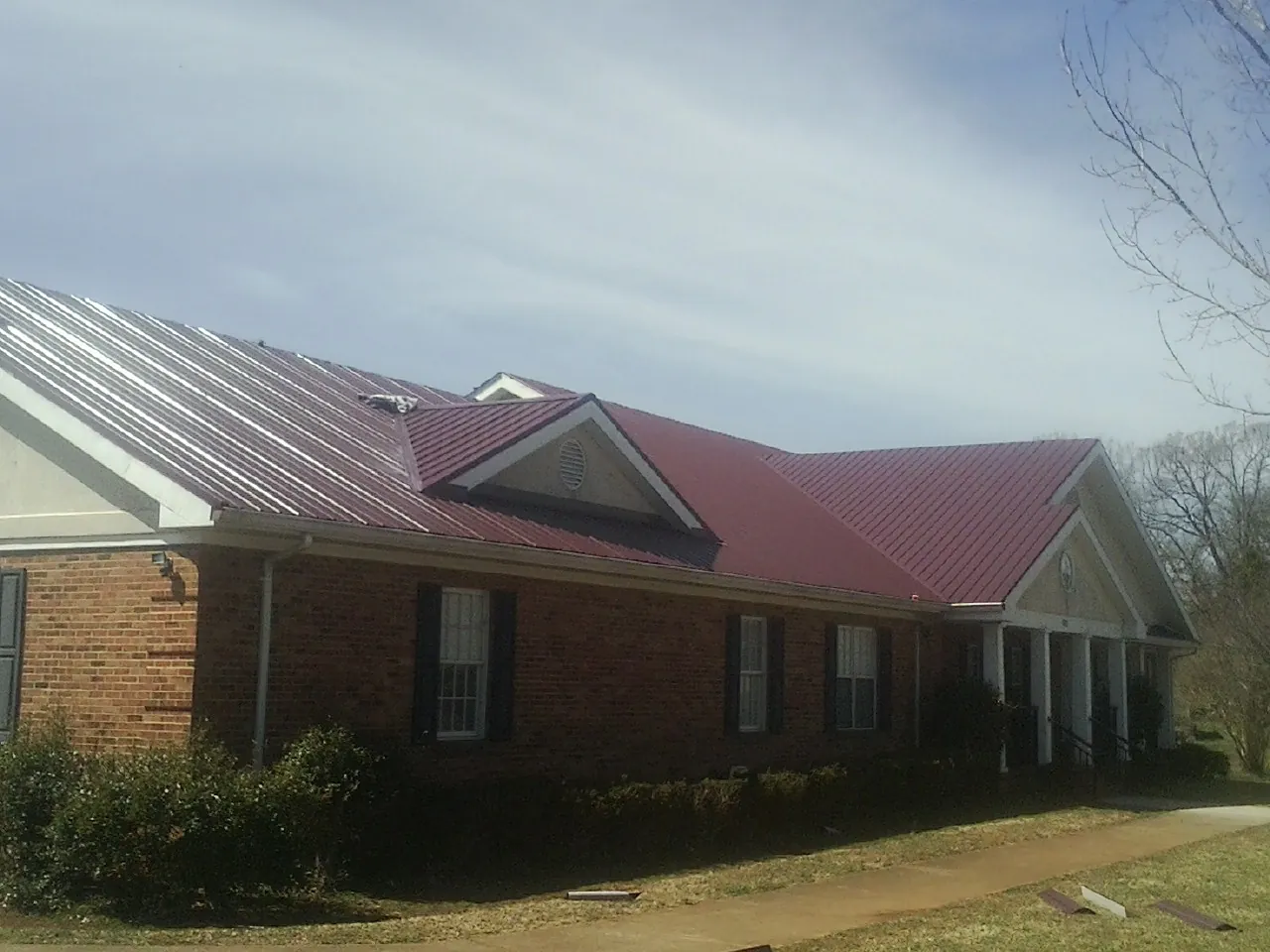 Red metal roof with gabled entries on a long brick building, from a Hail Damage Roof Repair job in Tyrone