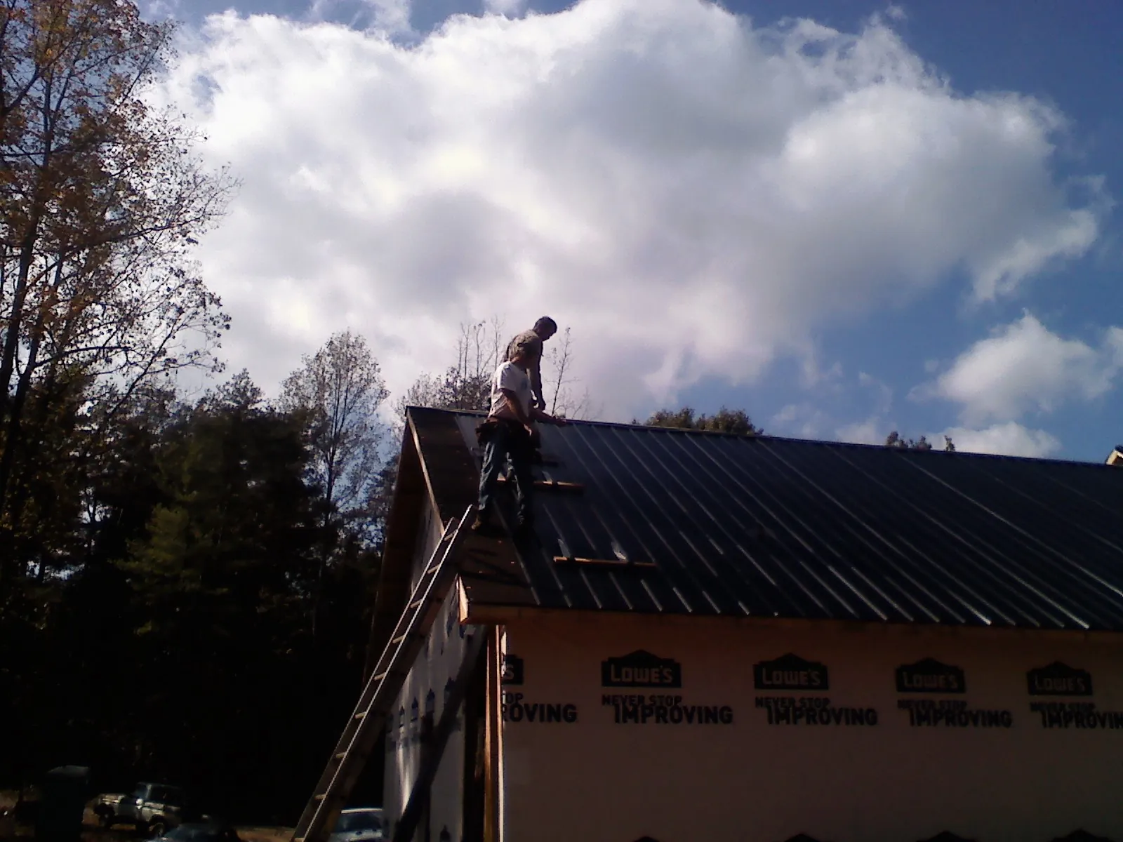 Roofer fastening dark metal panels high against a cloudy sky, from a Roof Inspection job in Tyrone