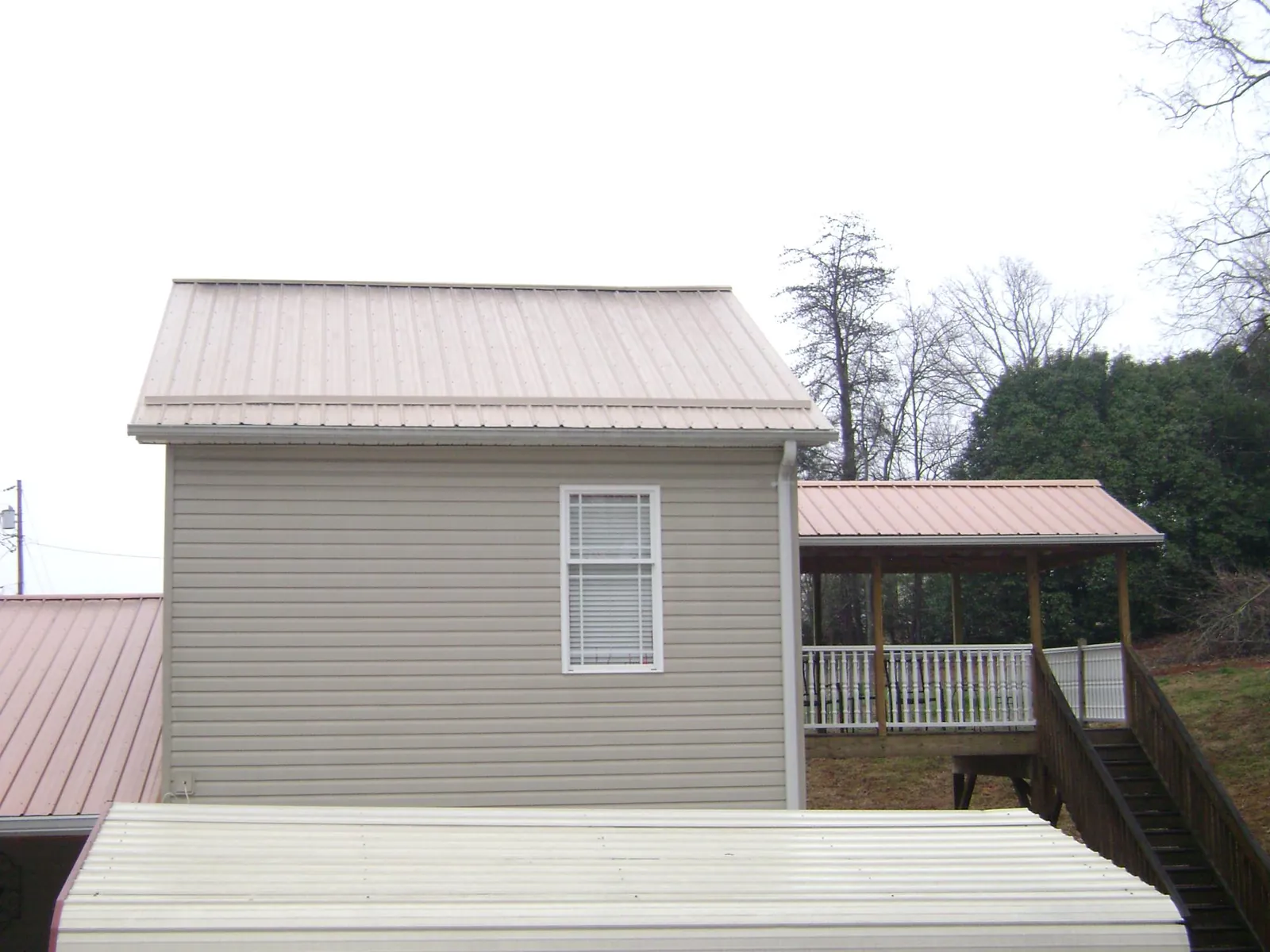 Tan metal roofs on a two story addition and attached porch, from a Roof Replacement job in Tyrone